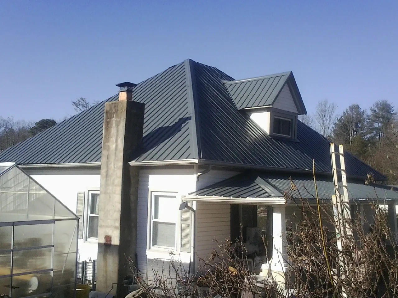 Dark blue standing seam metal roof on a white farmhouse with dormer — Slate & Tile Roof Repair by Roofing Brothers in Lakeside