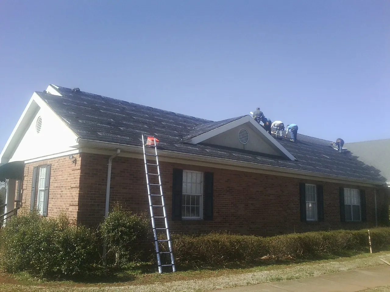 Crew tearing shingles off a brick ranch roof with a ladder set — Emergency Roof Repair work by our crew in Lakeside