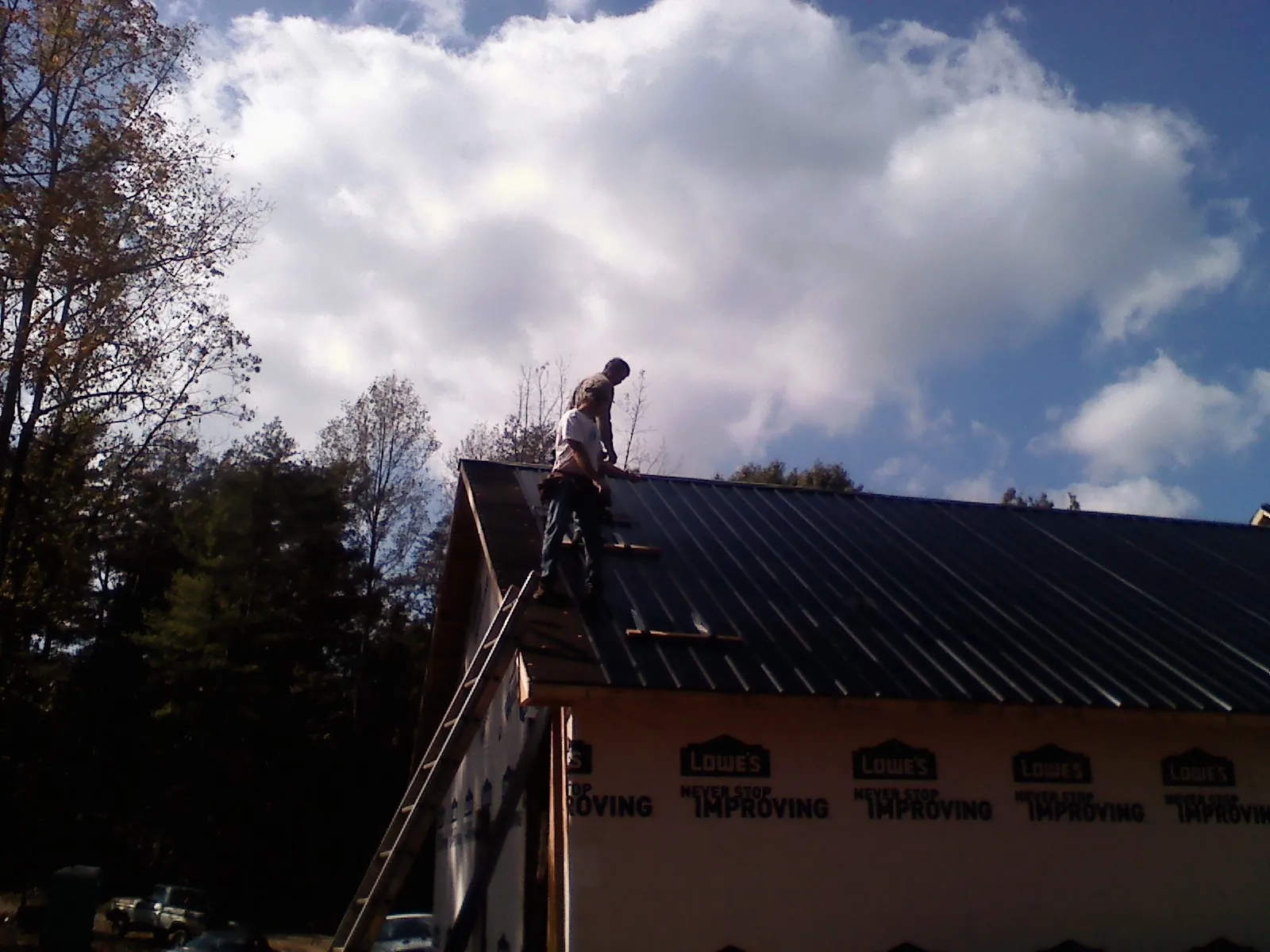 Roofer fastening dark metal panels high against a cloudy sky, from a Roof Inspection job in Lakeside